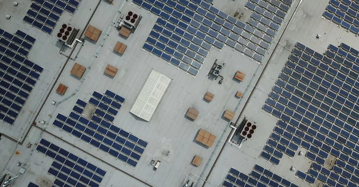 Prise de vue aérienne en plongée d'un vaste réseau de panneaux solaires sur le toit d'un bâtiment industriel.