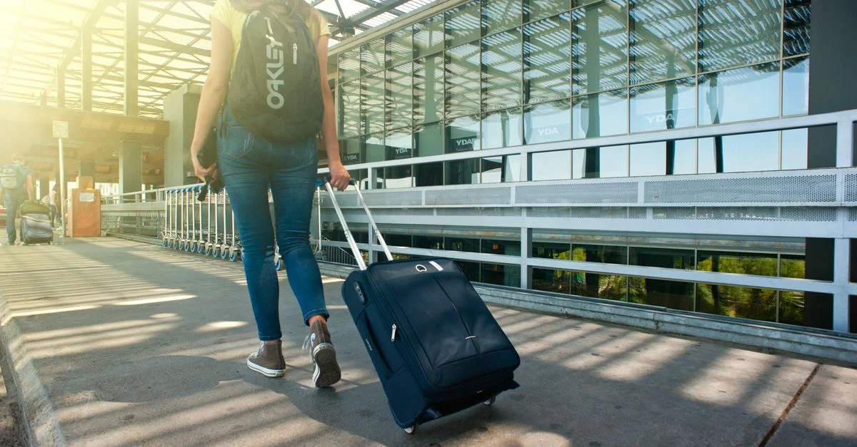 Une femme marche avec une valise devant un terminal d'aéroport, prête à voyager.