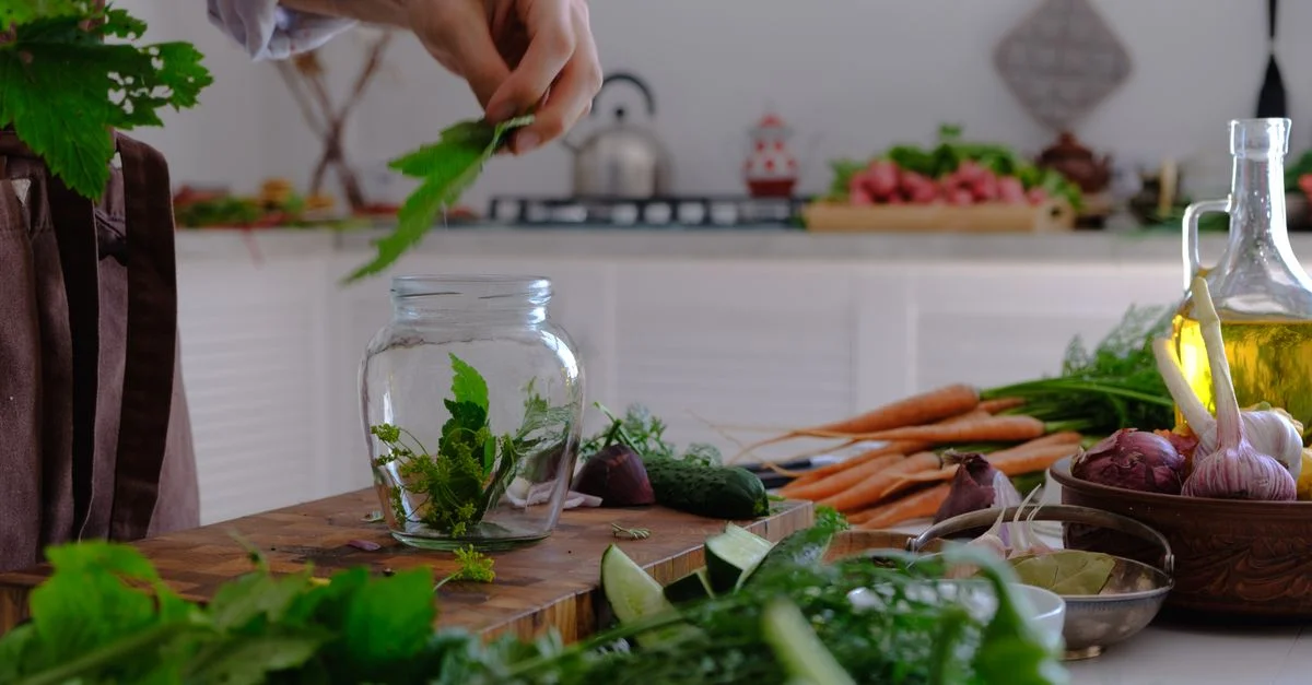 Main préparant des herbes et des légumes dans un environnement de cuisine. Ingrédients frais sur une table rustique.