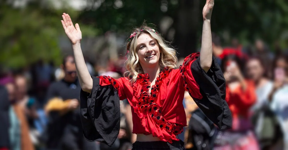 Une femme vêtue de rouge et de noir danse joyeusement lors d'un festival en plein air, entourée d'une foule.