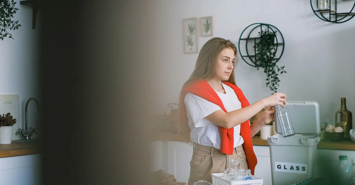 Jeune femme triant le verre pour le recyclage dans une cuisine moderne, promouvant des habitudes écologiques.